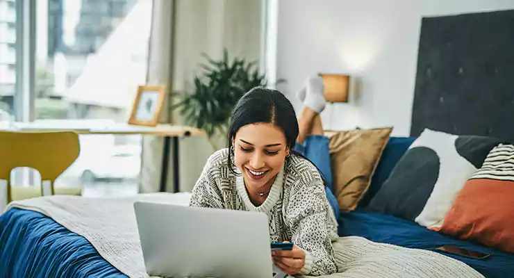 mulher mexendo no computador com um cartão de crédito em mãos