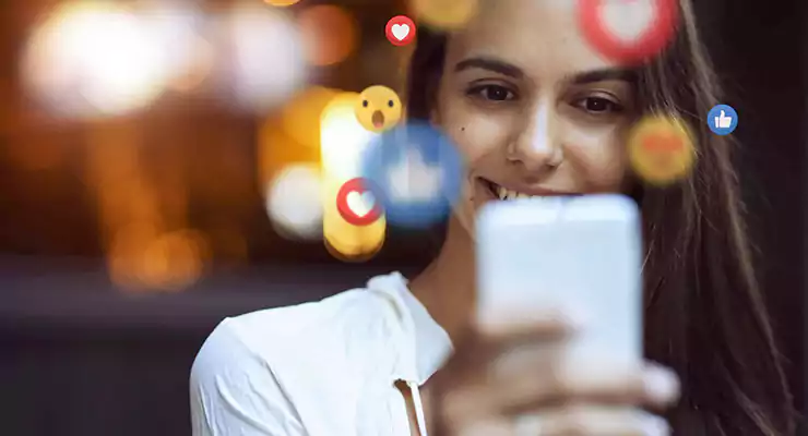 -conteudos-que-geram-mais-curtidas-nas-redes-sociais mulher mexendo no celular com itens de likes das redes sociais ao redor