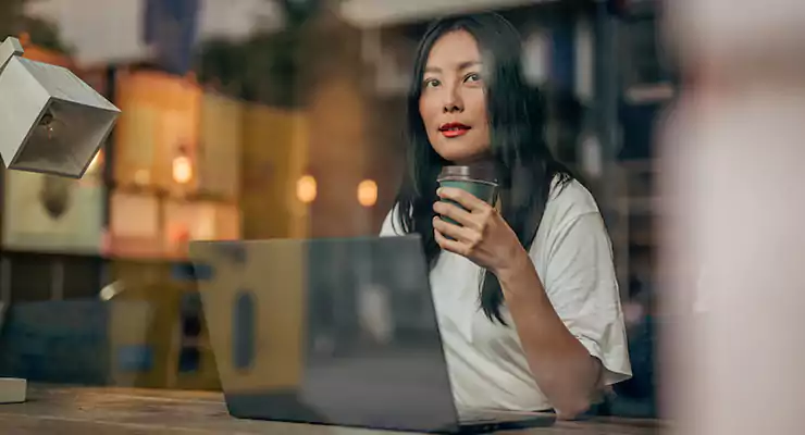 conheca-vantagens-de-investir-em-marketing-de-conteudo mulher nova pensativa tomando seu café enquanto trabalho no seu computador
