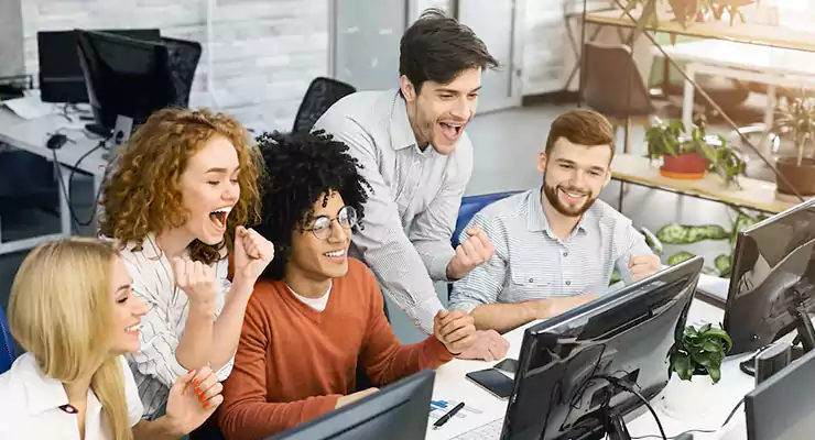 Colaboradores de uma agência reunidos e felizes em frente aos computadores