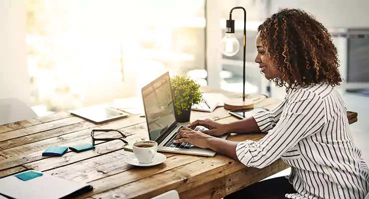 passo-a-passo-para-criar-o-blog-da-sua-empresa Mulher usando seu laptop em uma mesa de madeira
